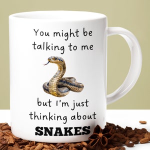 May include: White ceramic mug with a black snake illustration and the text "You might be talking to me but I'm just thinking about SNAKES".