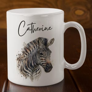 May include: White ceramic mug featuring a watercolour illustration of a zebra's head. The mug has the name "Catherine" written in black cursive on the front.