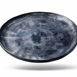 Pode incluir: Um prato de cerâmica azul escuro com uma superfície texturizada e uma borda ligeiramente elevada. O prato tem uma forma única e orgânica e um acabamento fosco. O prato tem aproximadamente 30 cm de diâmetro.