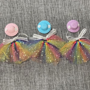 May include: Five rainbow tulle tutus with different colored hats. The hats are pink, light blue, purple, yellow, and pink. Each tutu has a white ribbon tied around it.