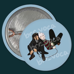 May include: A blue button with a cartoon image of two people, one with white hair and a red and white striped shirt, and the other with black hair and a black suit, both chained together.