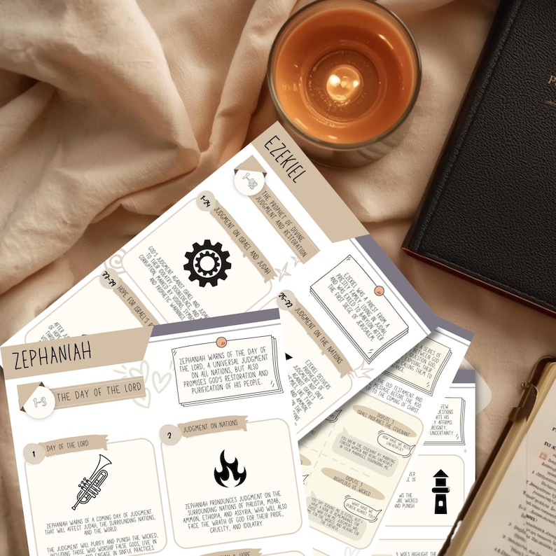 May include: A collection of Bible study cards with the text "Ezekiel" and "Zephaniah" visible. The cards feature illustrations and text, alongside a lit candle and a closed book.