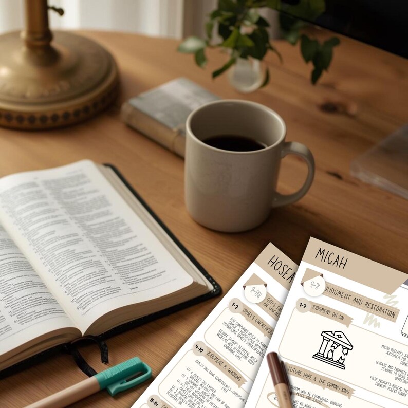 May include: An open Bible, a beige mug filled with coffee, and study notes are arranged on a wooden table. A green and a brown pen are also on the table. The notes are labeled "Hosea" and "Micah".