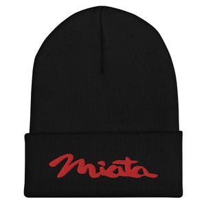 Puede incluir: Un gorro negro con la palabra "Miata" bordada en rojo. El gorro está hecho de un material de punto suave y tiene un dobladillo doblado.