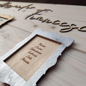 May include: Wooden wedding sign with names and a list of names in a decorative frame. The names "Alessandro" and "Francesca" are in cursive script. The frame contains the names: Marco, Laura, Sebastiano, Sabrina, Lida, and Marisa.