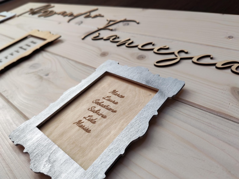 May include: Wooden wedding sign with names and a list of names in a decorative frame. The names "Alessandro" and "Francesca" are in cursive script. The frame contains the names: Marco, Laura, Sebastiano, Sabrina, Lida, and Marisa.