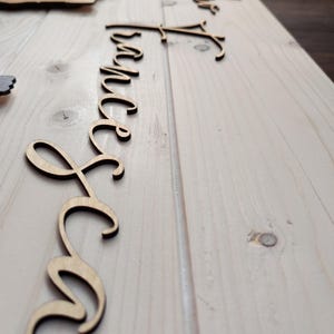 May include: Wooden laser-cut script words, including "Forever" and "Together", are arranged on a light-colored wooden surface. The words are in a cursive font, and the wood has a natural, unfinished appearance. The items are likely for wedding or home decor.