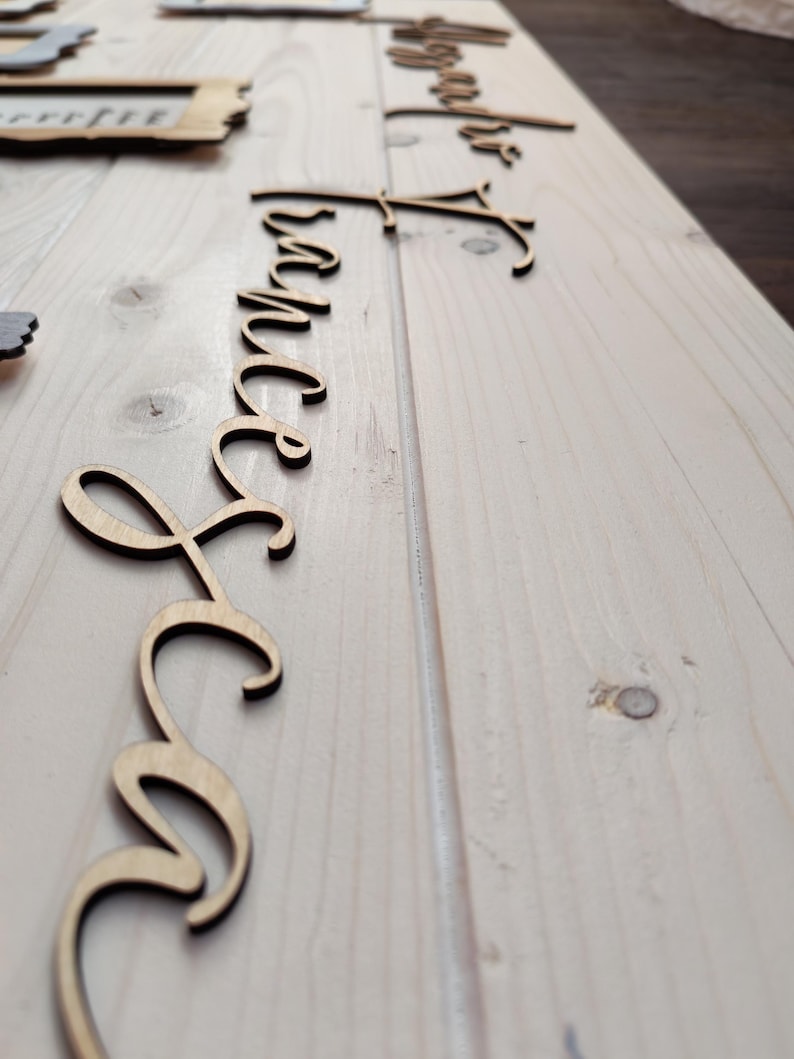 May include: Wooden laser-cut script words, including "Forever" and "Together", are arranged on a light-colored wooden surface. The words are in a cursive font, and the wood has a natural, unfinished appearance. The items are likely for wedding or home decor.