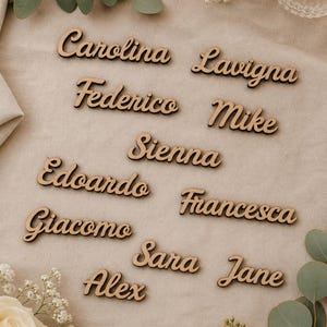 Peut inclure: Cartes de noms en bois avec des noms écrits en cursive. Les noms incluent Carolina, Lavigna, Federico, Mike, Edoardo, Sienna, Giacomo, Francesca, Alex, Sara et Jane. Les cartes sont marron clair avec un contour marron foncé.