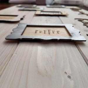 May include: Wooden framed signs with engraved text, arranged on a light wood surface. The frames have a dark gray border and a natural wood interior. The word "coffee" is engraved on one sign.
