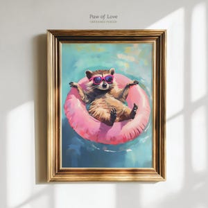 Könnte beinhalten: Gerahmter Kunstdruck mit einem Waschbären, der eine rosa Sonnenbrille trägt und auf einem rosa aufblasbaren Ring in einem Pool schwimmt. Das Kunstwerk trägt den Titel "Paw of Love" und ist ein ungerahmtes Poster. Der Rahmen ist goldfarben.