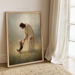 May include: A framed print showing a figure in white robes reaching out to a small dog. The artwork is bathed in soft light, with the text "Paw of Love" at the top. The frame is a light wood colour, creating a peaceful and heartwarming scene.