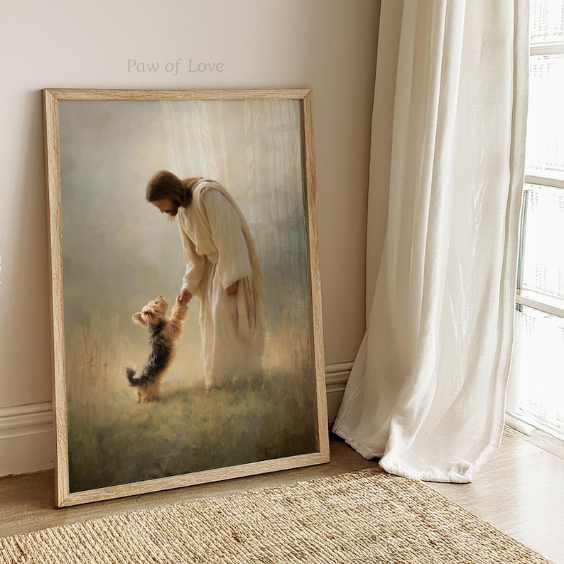 May include: A framed print showing a figure in white robes reaching out to a small dog. The artwork is bathed in soft light, with the text "Paw of Love" at the top. The frame is a light wood colour, creating a peaceful and heartwarming scene.