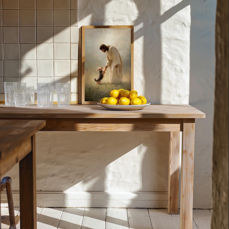 May include: A wooden table with a framed print showing a figure in white robes with a dog. A white plate holds several yellow lemons. Clear drinking glasses are arranged on the table. The text "Paw of Love" is visible.