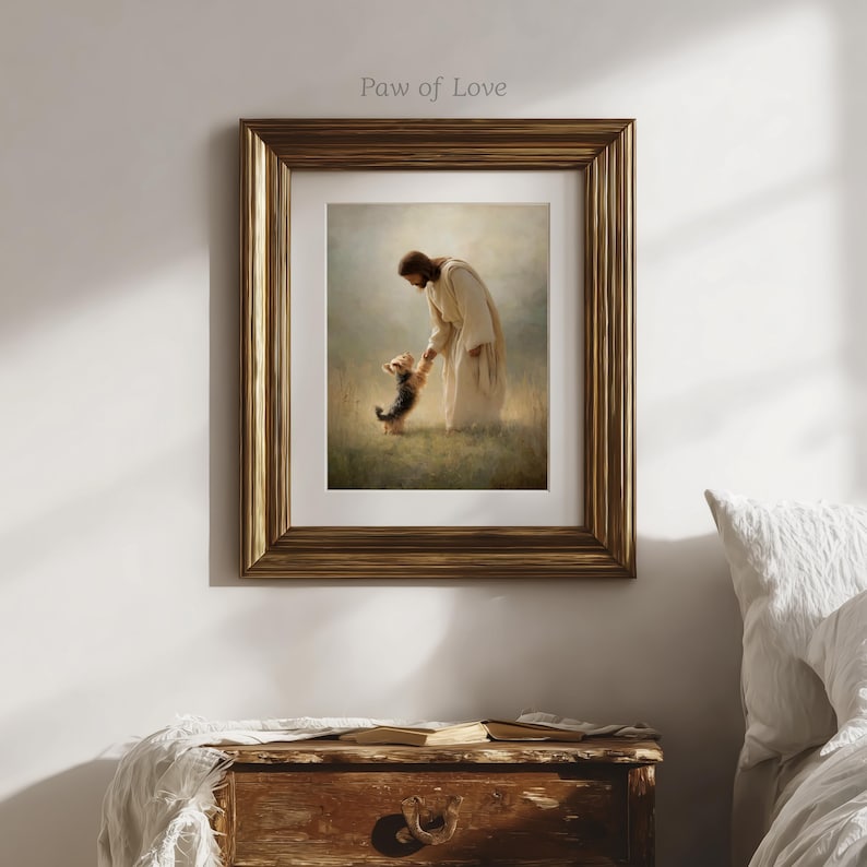 May include: Framed art print depicting a person in a white robe interacting with a small dog in a grassy field. The artwork is in a gold-coloured frame. The text "Paw of Love" is in the upper left corner.
