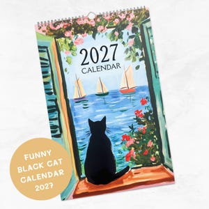 May include: A 2027 wall calendar featuring a painted illustration of a black cat sitting on a windowsill looking out at a blue sea with three sailboats. The scene is framed by green shutters and pink flowers. A circular beige sticker reads FUNNY BLACK CAT CALENDAR 2027.