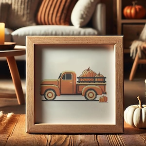May include: A framed cross-stitch design of an orange vintage pickup truck carrying pumpkins. The truck is on a white background with a brown wooden frame.