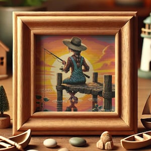 May include: A framed cross-stitch artwork depicting a person wearing a straw hat sitting on a wooden jetty fishing at sunset. The sky is a vibrant orange and pink, and the water is a calm blue.