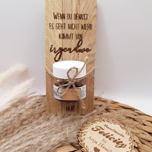 Könnte beinhalten: Ein Holzschild mit dem Text "WENN DU DENKST ES GEHT NICHT MEHR KOMMT VON irgendwo" und einem kleinen Glas Schokoladenaufstrich, das daran befestigt ist. Das Schild trägt auch den Text "HER!" und ein kleines Holzschild. Unter dem Schild befindet sich ein rundes Holzschild mit dem Text "Handmade Felicity by Anja Haucke".