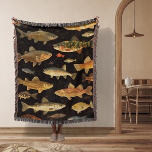 May include: A woven tapestry throw blanket featuring a dark background with a repeating pattern of colorful fish. The fish are depicted in a realistic style with intricate details.