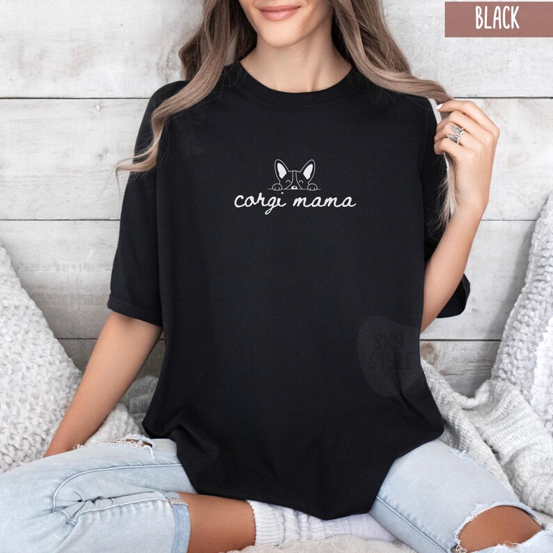 May include: Black t-shirt with a white outline of a corgi peeking over the top and the text "corgi mama" underneath.