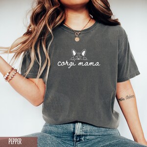 May include: A dark gray t-shirt with a white outline of a corgi peeking over the top and the text "corgi mama" underneath.