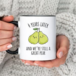K&ouml;nnte beinhalten: Wei&szlig;e Keramiktasse mit schwarzem Henkel und Rand, mit dem Text "4 YEARS LATER AND WE'RE STILL A GREAT PEAR" &uuml;ber einer Cartoon-Illustration von zwei l&auml;chelnden Birnen. Ein perfektes Geschenk zum Jahrestag.