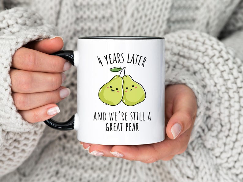 K&ouml;nnte beinhalten: Wei&szlig;e Keramiktasse mit schwarzem Henkel und Rand, mit dem Text "4 YEARS LATER AND WE'RE STILL A GREAT PEAR" &uuml;ber einer Cartoon-Illustration von zwei l&auml;chelnden Birnen. Ein perfektes Geschenk zum Jahrestag.