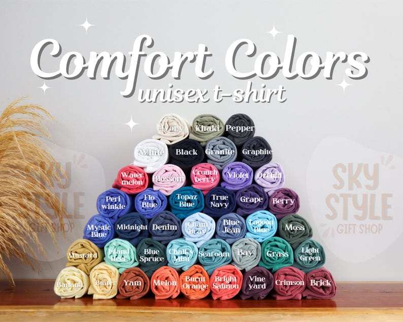 K&ouml;nnte beinhalten: Eine Pr&auml;sentation von gerollten Unisex-T-Shirts in verschiedenen Farben, darunter Wei&szlig;, Schwarz und Blau. Der Text "Comfort Colors unisex t-shirt" ist oben zu sehen. Die Shirts sind pyramidenf&ouml;rmig angeordnet und zeigen eine gro&szlig;e Auswahl an Farbt&ouml;nen.