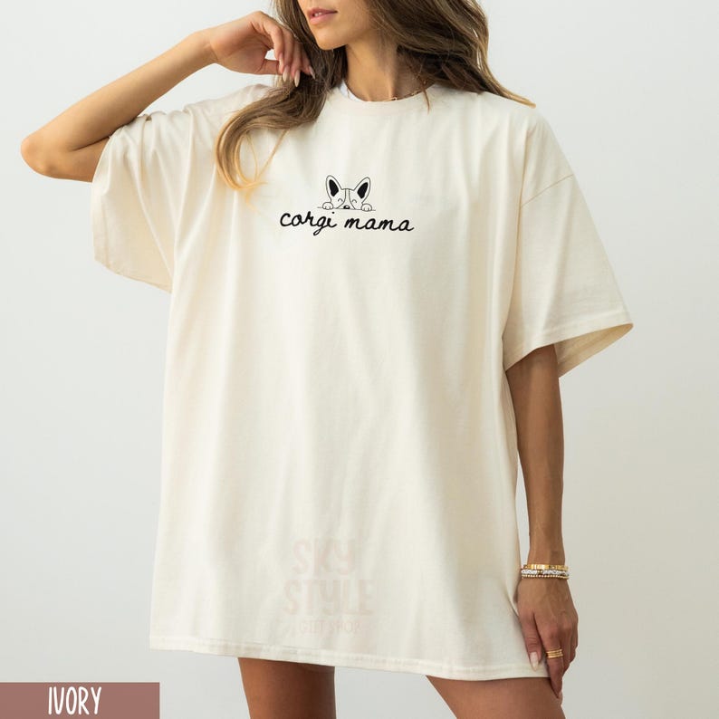 May include: A white oversized t-shirt with a black graphic of a corgi peeking over the top and the text "corgi mama".