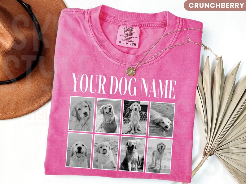May include: A bright pink short-sleeved t-shirt featuring the text YOUR DOG NAME in white capital letters above a grid of eight black and white photographs of dogs. The shirt has a crew neckline and a Comfort Colors brand label on the inside collar.