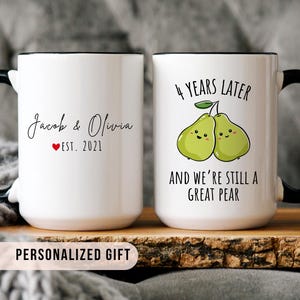 White ceramic mug set with black handles, featuring custom names and "Est. 2021" on one side, and two cute pears illustration with the phrase "4 years later and we’re still a great pear" on the other.