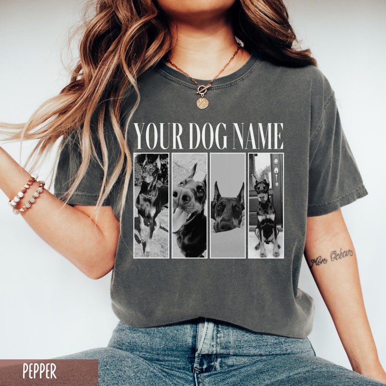 May include: A gray t-shirt with the text "YOUR DOG NAME" printed on the front. Four black and white photos of a dog are arranged in a row below the text. The dog is a Doberman Pinscher.