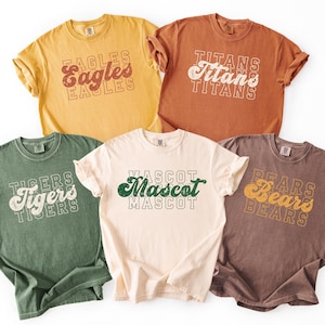 May include: Five short-sleeved t-shirts in various colors: yellow, orange, green, cream, and brown. Each shirt features a team name in a retro font: Eagles, Titans, Tigers, Mascot, and Bears. The shirts are likely made of a soft, comfortable material.