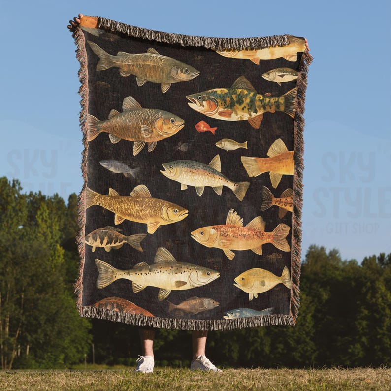 May include: A black woven throw blanket with a colorful pattern of various fish. The blanket features a variety of fish species, including trout, bass, and catfish, all rendered in a realistic style.