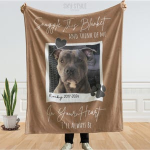 May include: A brown blanket with a photo of a dog, a black heart, and paw prints. The text on the blanket reads "Snuggle This Blanket And Think Of Me In Your Heart I'll Always Be". The dog's name is Rocky, and the years 2017-2024 are also printed.