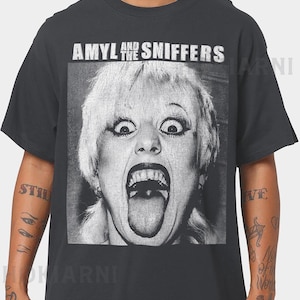 Puede incluir: Camiseta gris oscuro con una imagen en blanco y negro de una mujer con la boca abierta y la lengua fuera. El texto "AMYL AND THE SNIFFERS" está impreso encima de la imagen en letras blancas. Una camiseta de banda clásica.