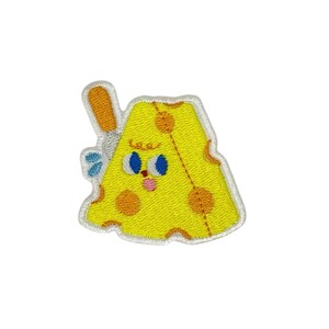 Könnte beinhalten: Ein gelber gestickter Patch in Form eines Käsekeils mit einem lächelnden Gesicht, zwei blauen Augen und orangefarbenen Punkten. Der Käse hat ein kleines orangefarbenes Messer, das aus der Oberseite herausragt.