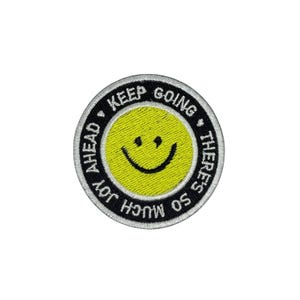 May include: Black and white embroidered patch with a yellow smiley face and the text "Keep Going There's So Much Joy Ahead".