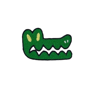 Könnte beinhalten: Grüner gestickter Alligator-Kopf-Patch mit gelben Augen und weißen Zähnen.