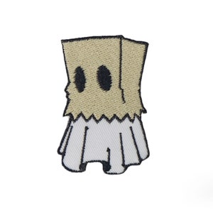 May include: Embroidered iron-on patch of a ghost wearing a brown paper bag over its head. The ghost has two black eyes and a white, ruffled skirt.