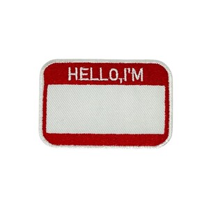 Puede incluir: Un parche rectangular bordado con borde rojo y las palabras "HELLO, I'M" en blanco. El centro es blanco, proporcionando espacio para un nombre. Adecuado para ropa o accesorios.