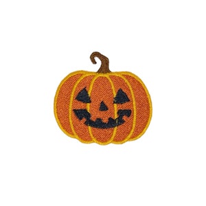 May include: A small orange pumpkin with a carved jack-o'-lantern face. The pumpkin is embroidered with a black face and has a brown stem.