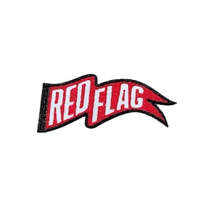 Puede incluir: Parche bordado en forma de bandera roja con las palabras "RED FLAG" en letras blancas. La bandera tiene un borde negro y está sobre un fondo blanco. Ideal para ropa o accesorios.