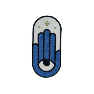 May include: A blue and white embroidered patch featuring a hamsa hand design with an eye in the centre. The hamsa hand is a symbol of protection and good luck.