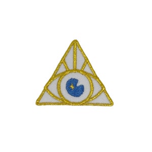 May include: A white triangle with a gold outline and a blue eye with a gold star inside. The eye is in the center of the triangle.