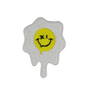 May include: A white embroidered patch shaped like a fried egg with a yellow smiley face in the yolk. The smiley face has an 'X' for eyes.
