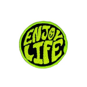 May include: A round, black and neon green embroidered patch with the text "ENJOY LIFE" in a retro font.