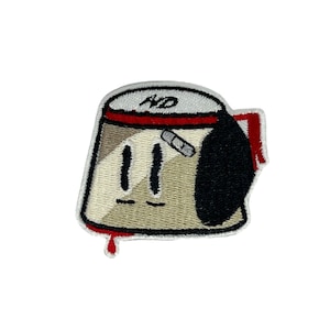 Puede incluir: Parche bordado de una cafetera turca de dibujos animados con una banda roja alrededor de la parte superior, un vendaje blanco en el lateral y un asa negra. La cafetera tiene una cara sonriente con dos ojos y una pequeña boca.