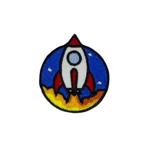 May include: A white rocket with red flames and a blue background. The rocket is in a circle with stars.